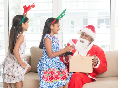 Happy Indian family celebrating Christmas holidays, with gift box and santa sitting on couch at home, Asian people festival mood indoors. 