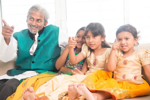 Portrait of Indian family watching movie at home, all finger pointing away. Happy Asian father and children indoors lifestyle.