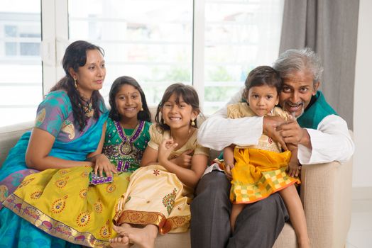 Portrait of happy Indian family sitting on couch at home. Asian people indoors lifestyle.