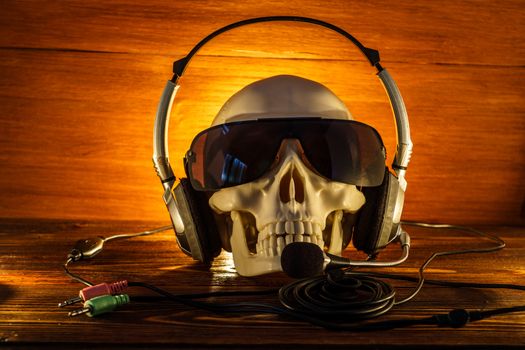 Skull in glasses and with headphones on an old wooden background. A human skull lit by candles on  wooden floor, the concept of Halloween.
