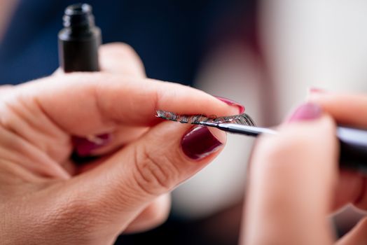 Close-up of a preparing false eyelashes with a cosmetic glue for applying to model.