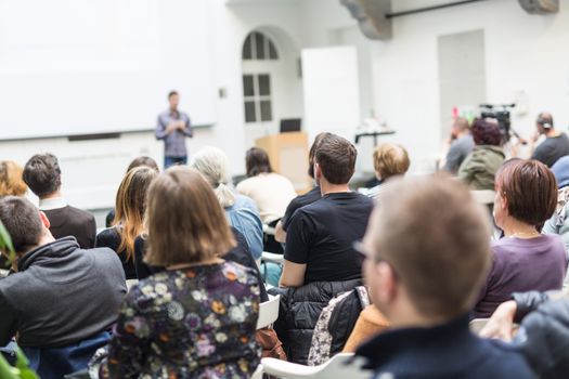 Male speaker giving presentation in lecture hall at university workshop. Audience in conference hall. Rear view of unrecognized participant in audience. Scientific conference event.