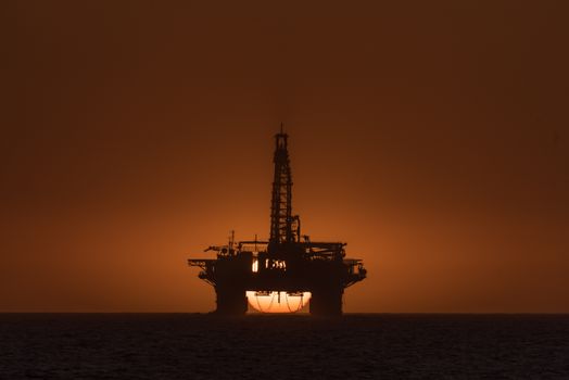The sun is setting behind an oil drilling platform anchored in the Atlantic Ocean at Longbeach in the Namib Desert of Namibia