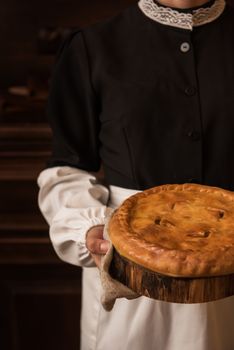 Pie from potato meat cheese and vegetables. Freshly baked pie in hands of woman in uniform