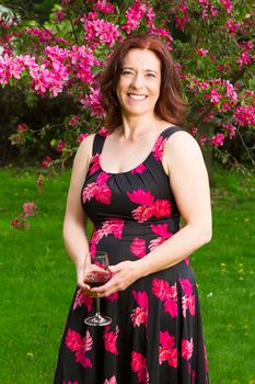 forty something brunette woman wearing a sun dress holding a glass of wine under a cherry tree