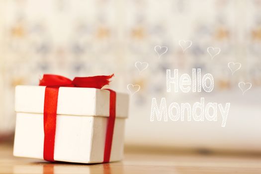 hello monday message with white gift box with red ribbon on wood background