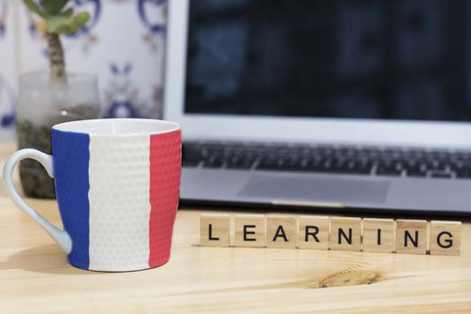 french  flag painted on cup coffee, letter wood learning,gray laptop