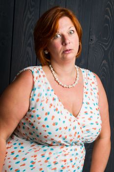 forty year old woman wearing a summer dress, in front of a blue stain wood panel background, with a annoyed expression