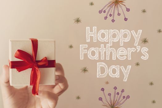 hand holding white gift box with red ribbon and happy father's day message decorated with watercolor flowers