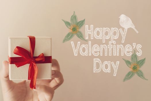 Happy Valentine's day message with white gift box with red ribbon hold on hand woman