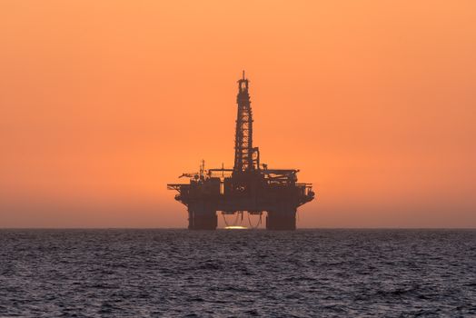The sun is setting behind an oil drilling platform anchored in the Atlantic Ocean at Longbeach in the Namib Desert of Namibia