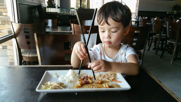 Cute Young Chinese and Caucasian Boy Learning To Use Chopsticks At Restaurant.