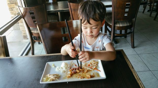 Cute Young Chinese and Caucasian Boy Learning To Use Chopsticks At Restaurant.