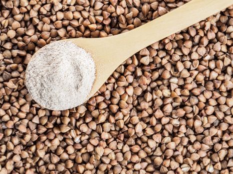 Buckwheat flour in wooden spoon and buckwheat grains. Whole-grain buckwheat flour on buckwheat grains background. Copy space. Top view or flat lay.