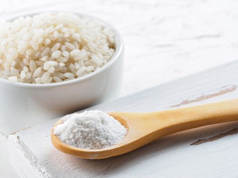rice flour in wooden spoon and rice grains on white background. Copy space.