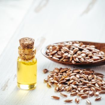 Brown flax seeds in spoon and flaxseed oil in glass bottle on white wooden background. Flax oil is rich in omega-3 fatty acid. Copy space. Square