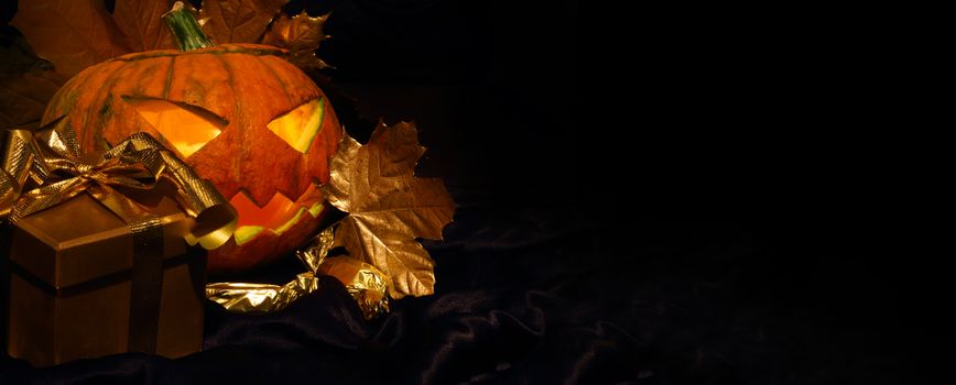 Halloween pumpkin with autumn leafs and gift on black