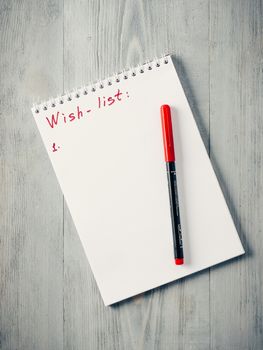 Christmas gifts shopping planning. Make shopping, wish list or to-do list for Christmas. Notebook with red pen on gray wooden background. Copy space. Top view or flat lay.