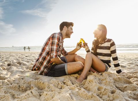 Young couple at the beach having fun, laughing and drinking beer