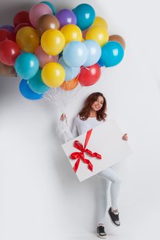 Young smiling woman with balloons and big gift box