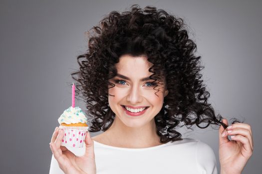 Beautiful young woman holding small cake with colorful candle. Birthday, holiday. Studio portrait
