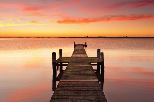 Stunning vivid red sunrise and timber jetty with reflections of the beautiful sky in the waters.  
Gorokan jetty, Australia