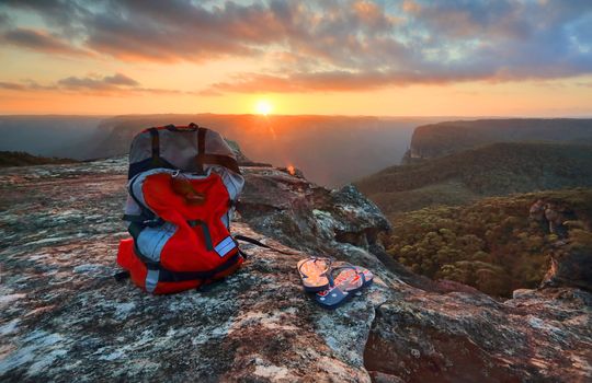 Sunset from a rocky outcrop of the Explorers Range, Blue Mountains Australia.  A  backpack and thongs with Australian flag sit catch the last light of the setting sun pver the Pierces Pass and Govets Gorge arm of the Grose Valley.