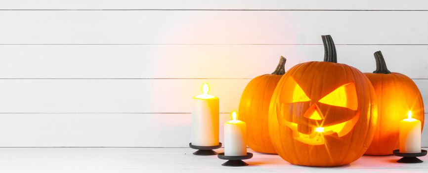 Halloween pumpkin head jack lantern and candles on white wooden background