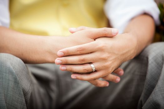 Close up of an Asian groom's hands showing wedding ring and wearing a yellow vest and grey pants.