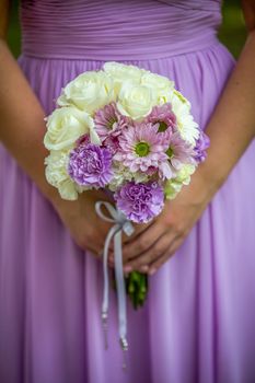 Bridesmaid holding bouquet with white, purple, and lavender flowers.