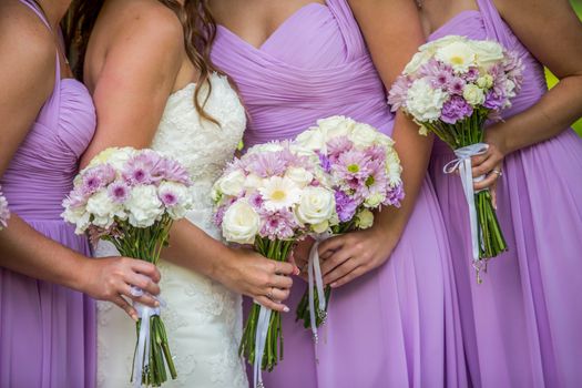A bride and three bridesmaids wearing lilac or purple dresses holding a beautiful arrangement of lavender and white bouquets.