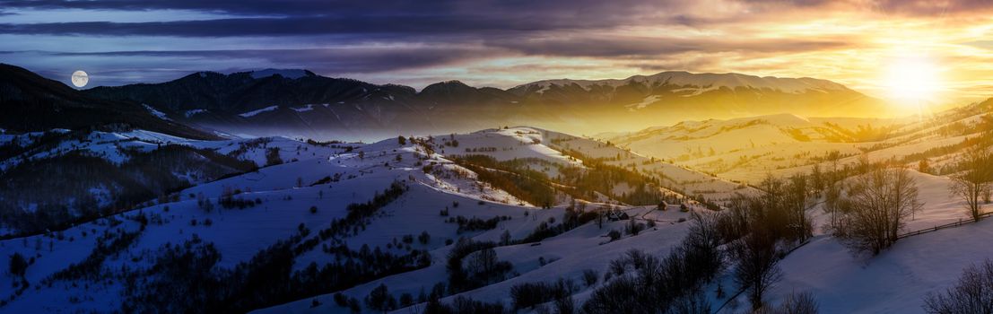 day and night time change concept in gorgeous panorama of mountainous countryside in winter. snow covered rural area on rolling hills and huge mountain ridge in a distance. fantasy world