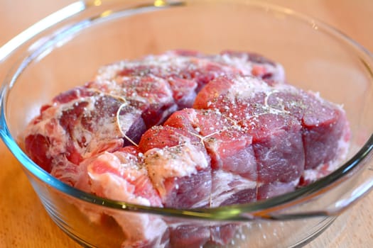 Two pieces of raw pork necks ready for baking in glass baking dish.