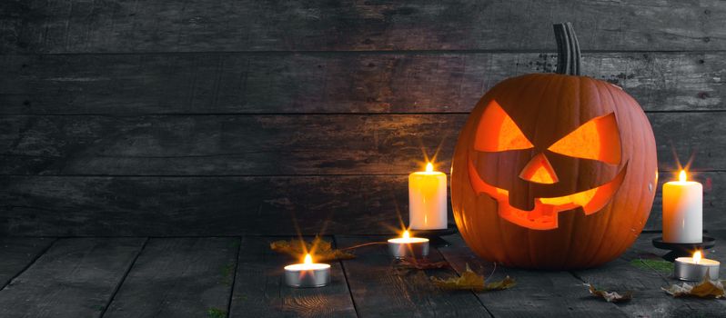 Halloween pumpkin head jack o lantern and candles on wooden background