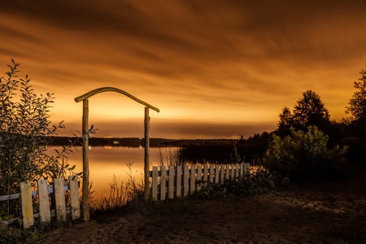 Night landscape. A fence before a pond and the night city on the horizon