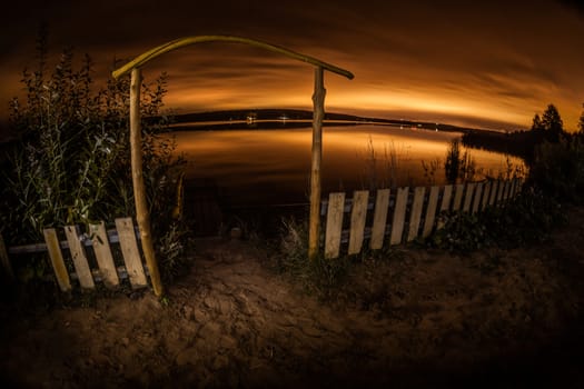 Night landscape. A fence before a pond and the night city on the horizon