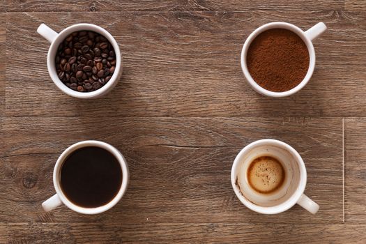 Variety of cups of coffee and coffee beans on old wooden table. Four cups of coffee, phases of drink - bean, ground and empty cup