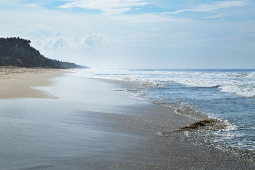 The long ocean beach is in the horizon with small waves and haze.