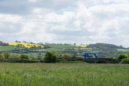 a double deck bus on a bridge in the couintryside passes fields