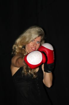 funny blonde girl in black casual dress in red boxing gloves