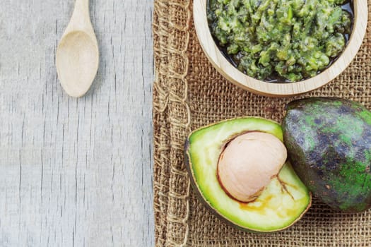 Avocado in a bowl and half cut on wooden floor.