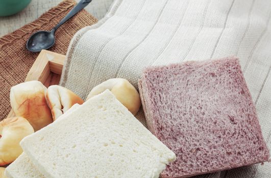 Many breads and cups of coffee on a tablecloth.