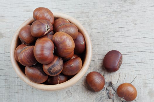 Chestnuts roasted in a bowl on wooden floor.