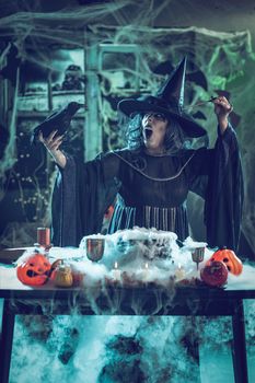Witch with awfully face in creepy surroundings and blackbird in her hand send messages to dead. Halloween concept.