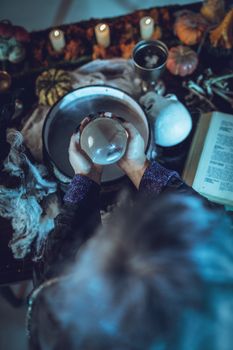 Top view of a magic ball in witch's hands above pot with poison potion.