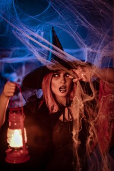 Witch with lighted lantern in her hand in creepy cobweb surroundings is looking for saomething.