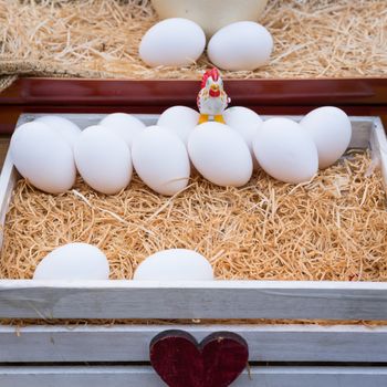 White chicken eggs leaning on straw in wooden basket