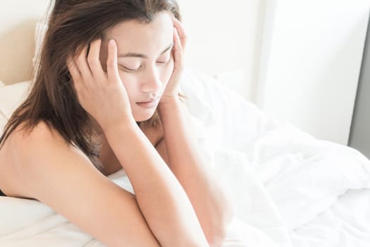 Closeup woman waking up with sore head on bed, health care and medical concept, selective focus