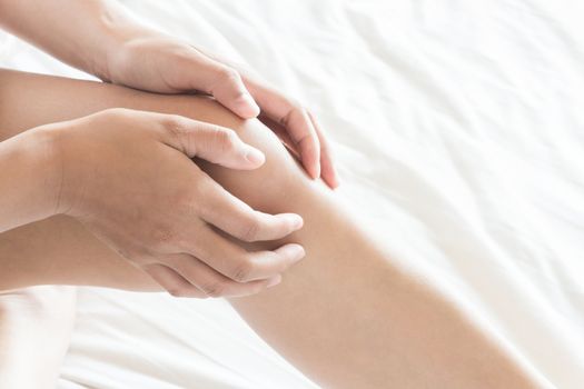 Closeup woman hand holding knee with pain on bed, health care and medical concept