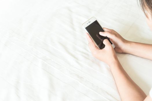 Closeup young woman holding smart phone lying on bed, happy and relax time concept